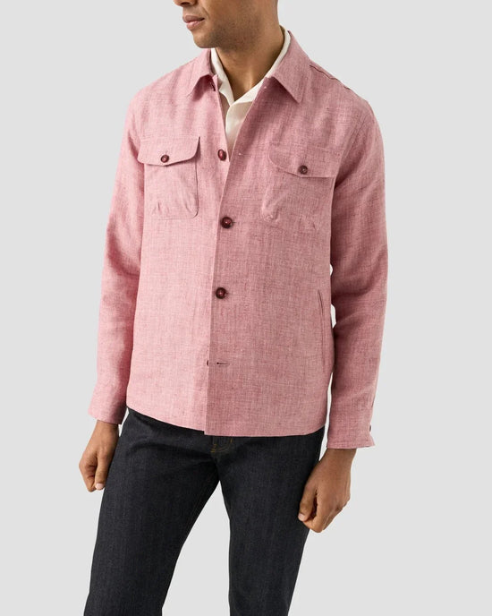 Herr i rosa linneoverskjorta med fyra fickor, vit skjorta och mörka jeans mot ljus bakgrund