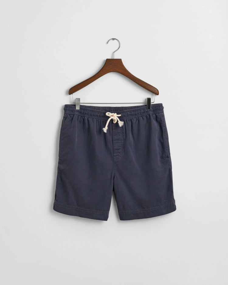Marinblå herrshorts med dragsko, klassiska sommarshorts på galge mot vit bakgrund.