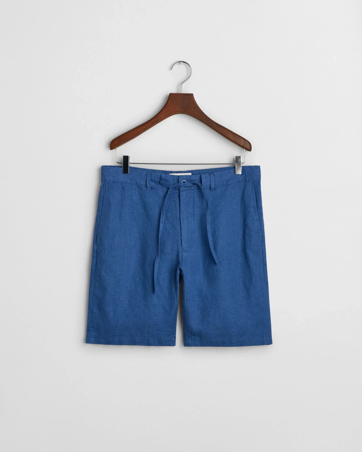 Blå herrshorts i lin med bälte, hänger på galge mot vit bakgrund.