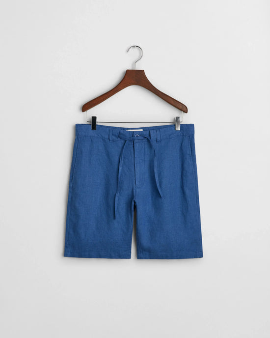 Blå herrshorts i lin med bälte, hänger på galge mot vit bakgrund.
