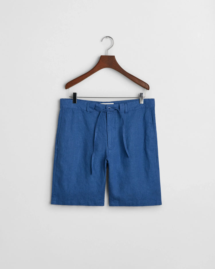 Blå herrshorts i lin med bälte, hänger på galge mot vit bakgrund.