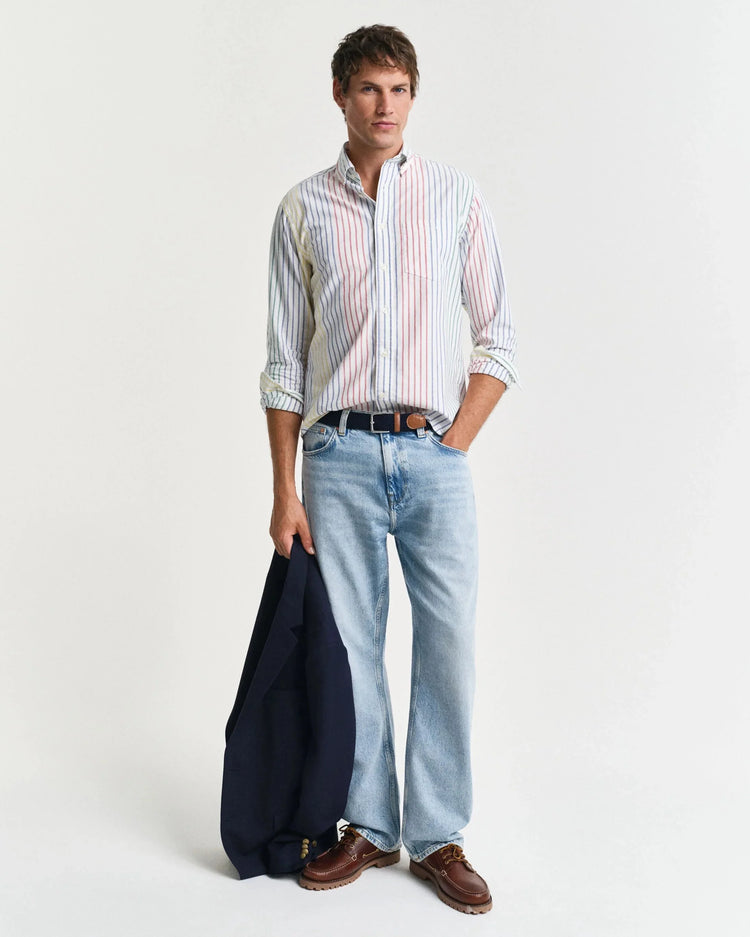 Man i randig skjorta och ljusa jeans, håller en marinblå kavaj, klassisk herrstil