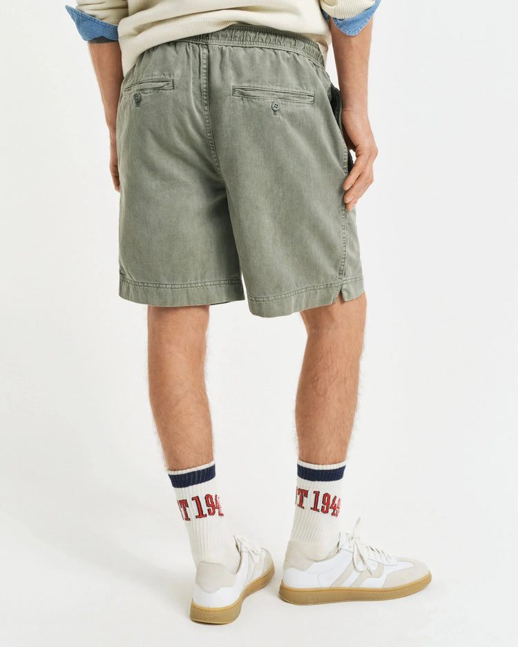 Herrmodell i gröna shorts, vita sneakers och strumpor med tryck, bakifrån
