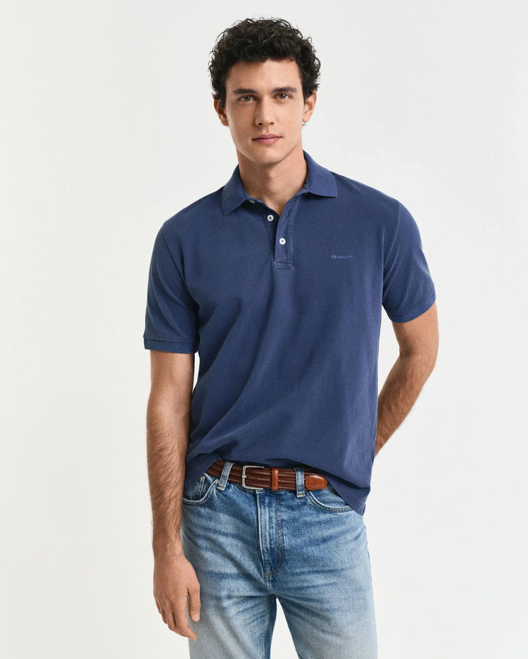 Man i blå pikétröja och ljusa jeans, klassisk herrstil mot vit bakgrund