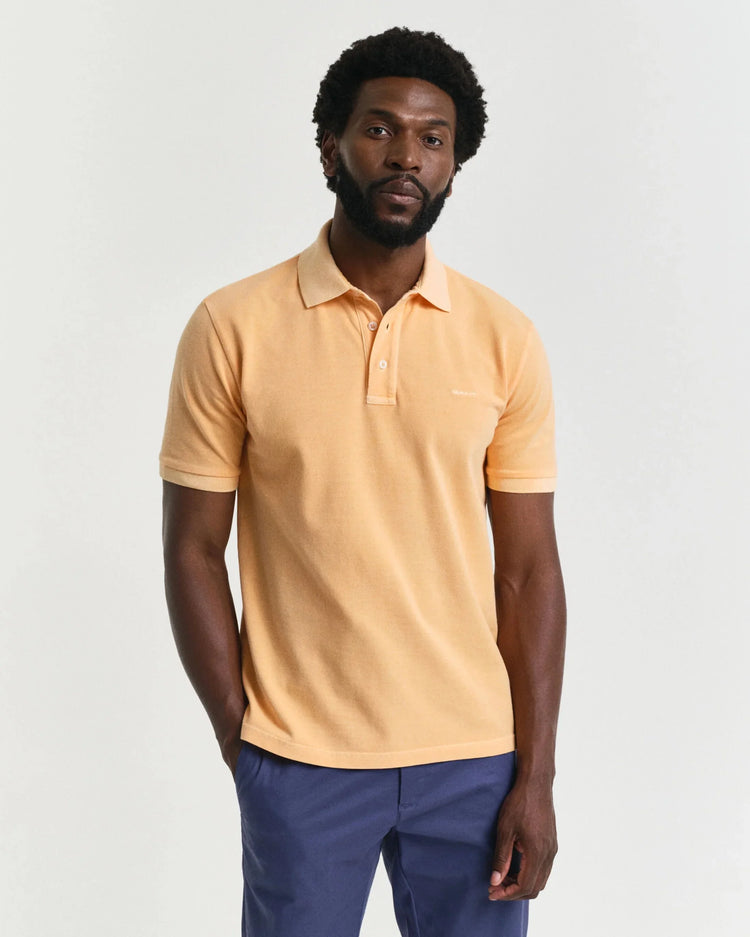 Man i ljusgul pikétröja och blå chinos mot vit bakgrund, klassisk herrstil.