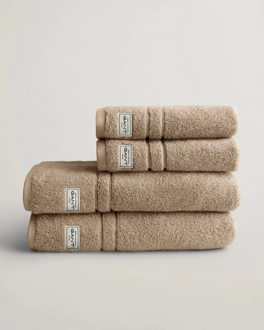 Beige handdukar i frotté staplade på varandra mot vit bakgrund, lyxigt badrumstillbehör.