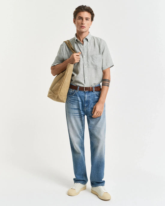 Man i kortärmad skjorta, blå jeans, sneakers och väska på vit bakgrund, herrmode