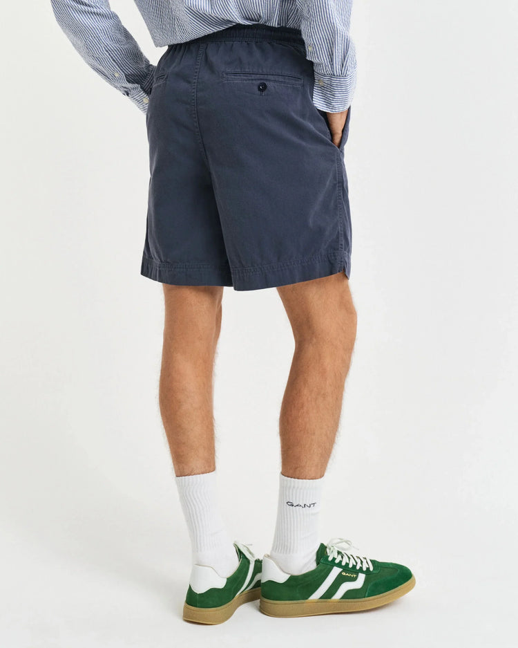 Herrmodell i mörkblåa shorts, randig skjorta, vita strumpor och gröna sneakers