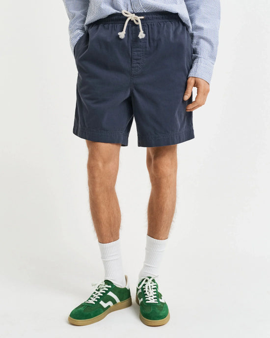 Marinblå herrshorts med dragsko, vit- och blårandig skjorta, gröna sneakers.