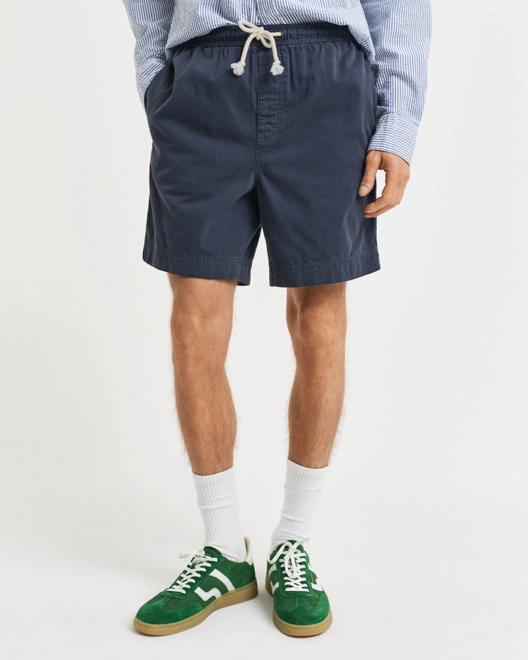 Marinblå herrshorts med dragsko, vit- och blårandig skjorta, gröna sneakers.