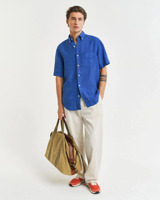 Man i blå linneskjorta och beige byxor med weekendväska, herrmode sommarstil
