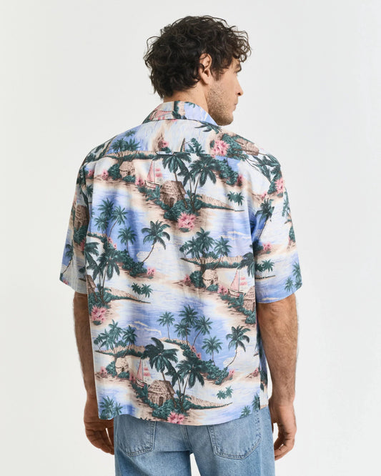 Man i mönstrad hawaiiskjorta med strandmotiv, ljusa denimjeans, sett bakifrån