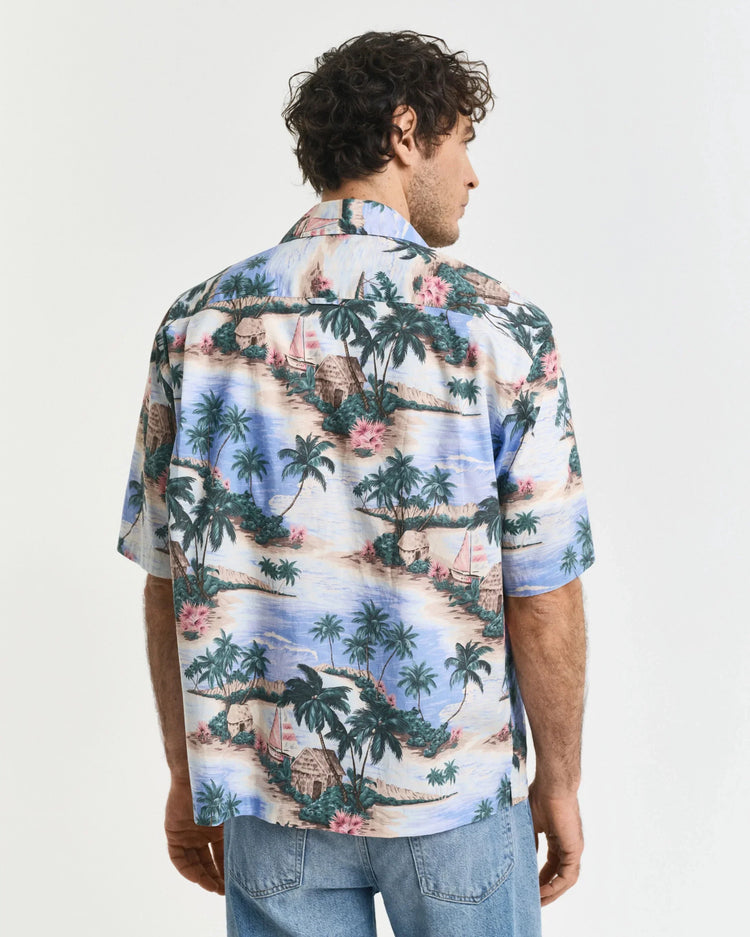Man i mönstrad hawaiiskjorta med strandmotiv, ljusa denimjeans, sett bakifrån