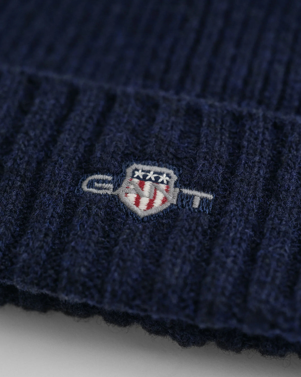 Detalj av marinblå herrmössa i ull med broderad emblem, ribbstickad design