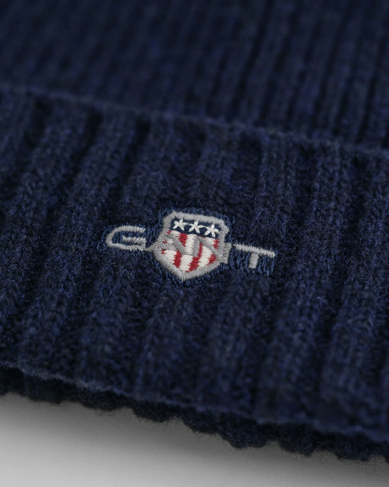 Detalj av marinblå herrmössa i ull med broderad emblem, ribbstickad design