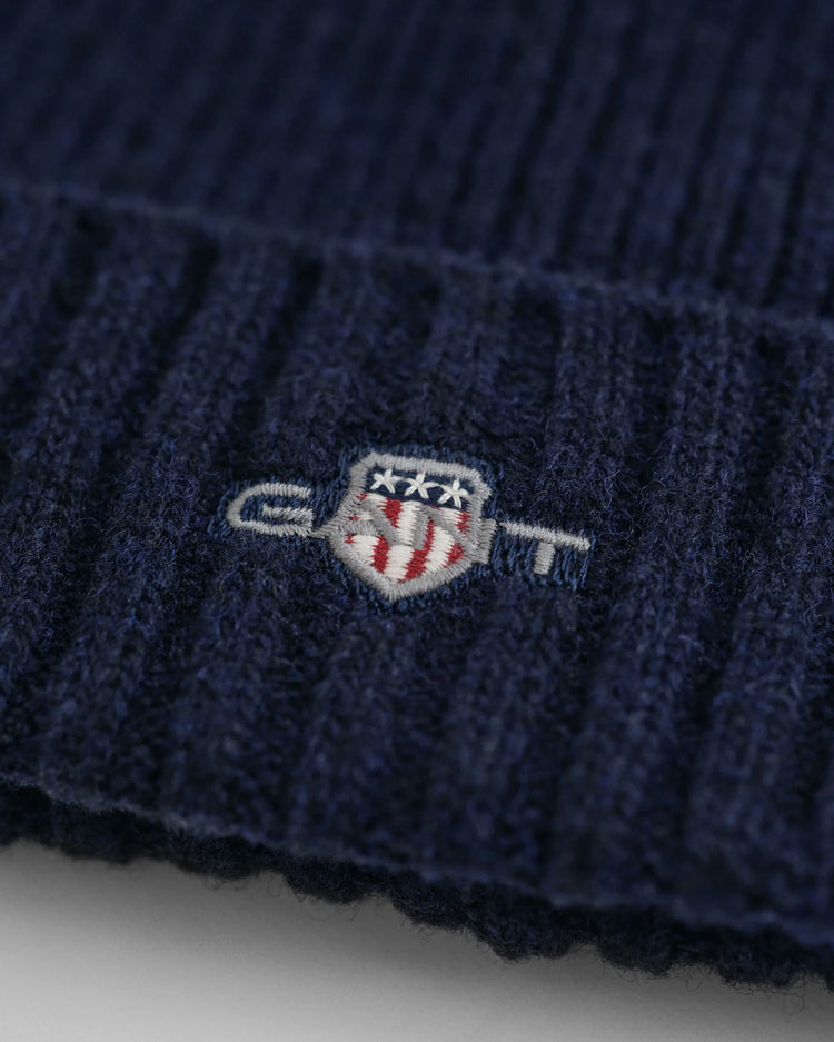 Detalj av marinblå herrmössa i ull med broderad emblem, ribbstickad design