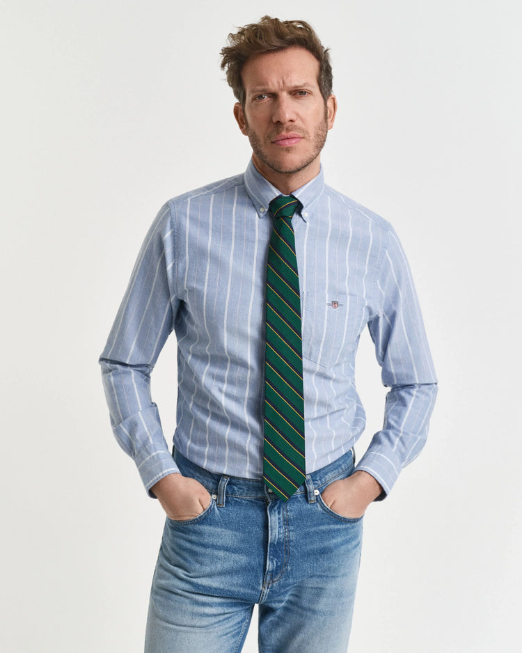 Man i blå randig skjorta, grön slips och jeans mot vit bakgrund, klassisk herrstil