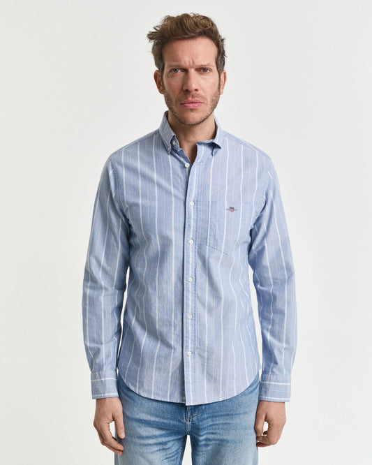 Man med klassisk ljusblå randig skjorta och jeans, stilren herrklädsel mot vit bakgrund.
