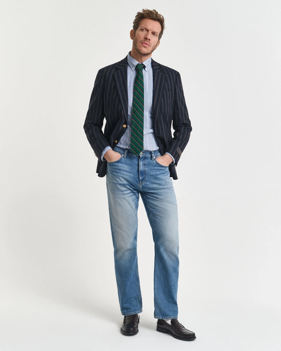 Man i randig kavaj, slips, skjorta och jeans på vit bakgrund, klassisk herrstil.