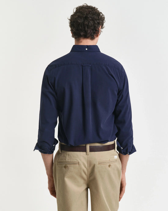 Herr i mörkblå skjorta och beige chinos, klassisk herrmode mot vit bakgrund