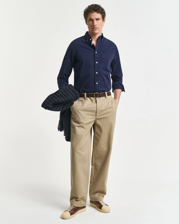 Man i marinblå skjorta och beige byxor med sneakers, klassisk herrstil på vit bakgrund