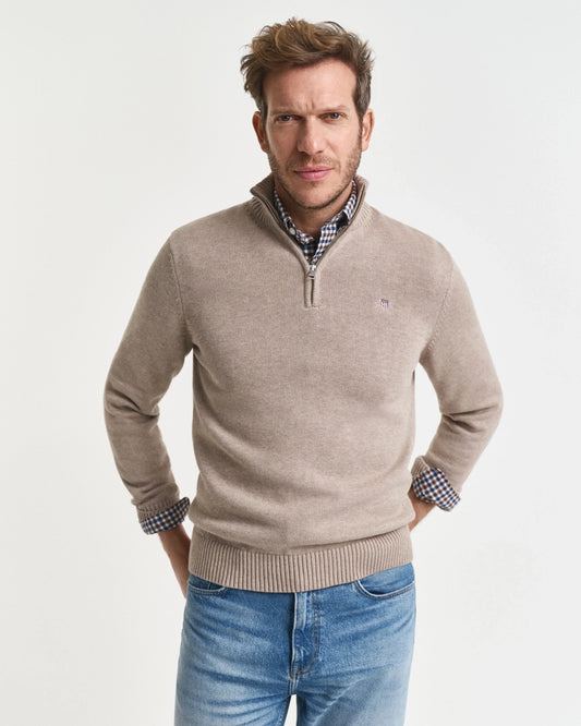Man i beige halvzip-tröja och rutigt skjort stående mot vit bakgrund, herrmode