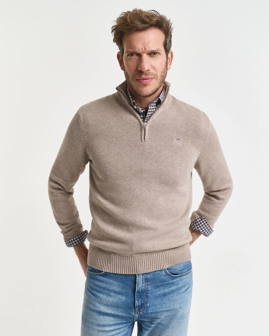 Man i beige halvzip-tröja och rutigt skjort stående mot vit bakgrund, herrmode