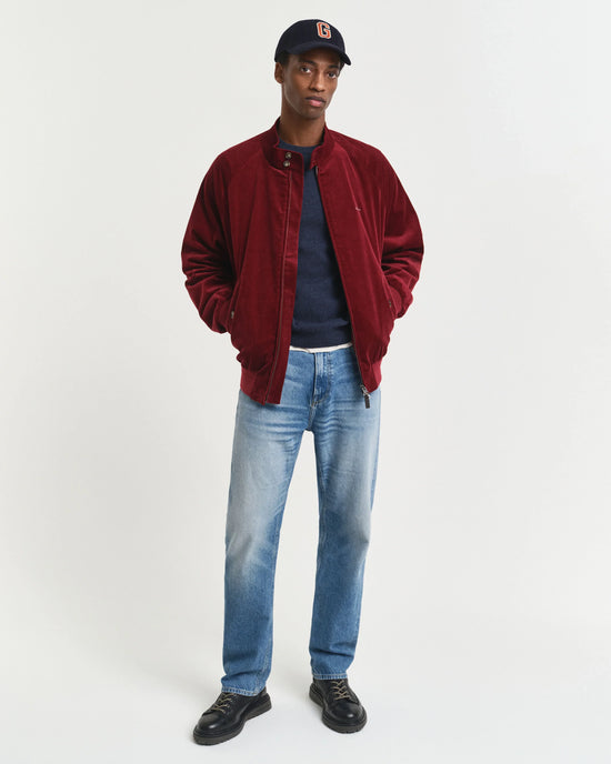 Modell bär herr jacka, röd, med jeans och mörka skor mot vit bakgrund