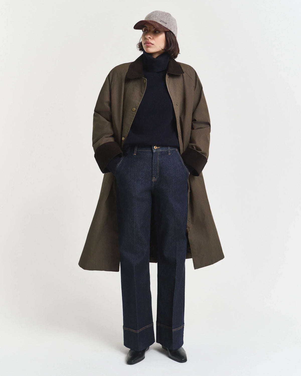 Olivgrön långrock herr, mörkblå polotröja, blå raka jeans, beige keps