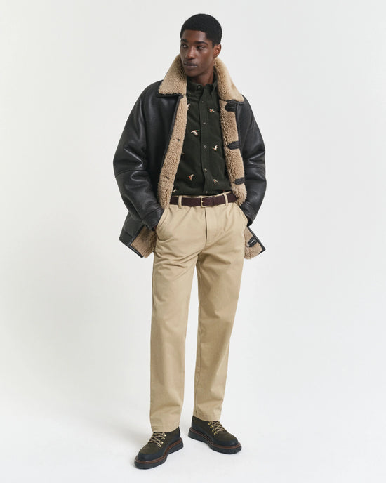 Modell i beige herrbyxor, mörk skjorta och skinnjacka med fårskinnskrage.