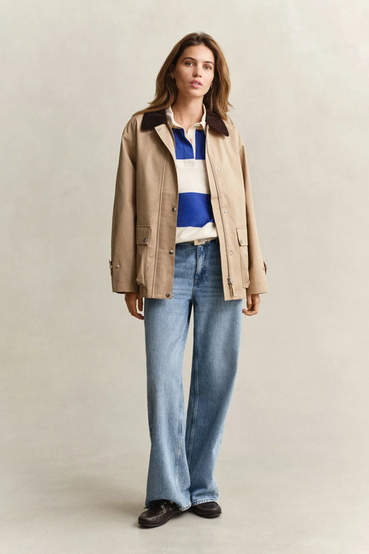 Beige jacka med mörk krage, blåvit randig rugbytröja, ljusa raka jeans