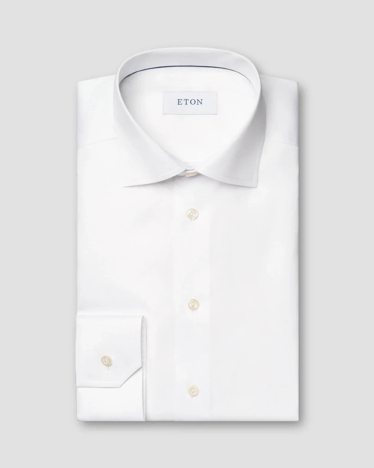 Vit dresskjorta i twill med klassisk krage och knappar, vikt mot grå bakgrund.