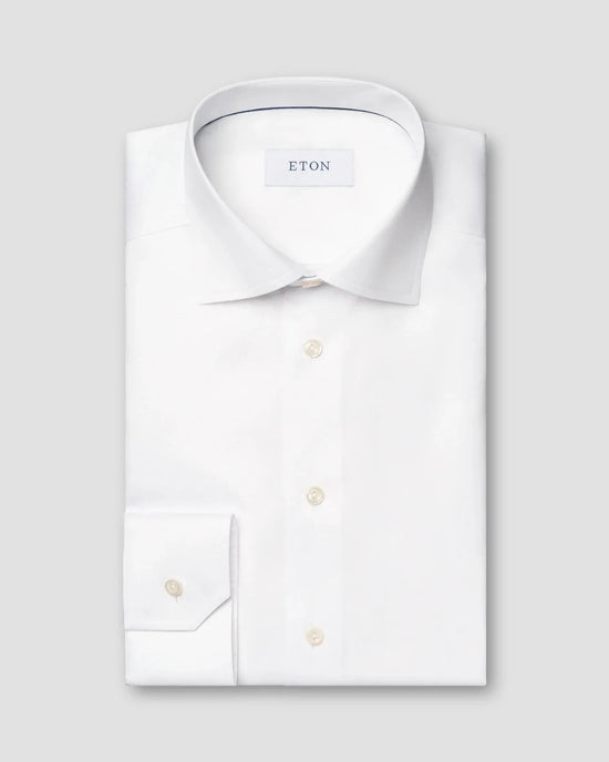 Vit dresskjorta i twill med klassisk krage och knappar, vikt mot grå bakgrund.