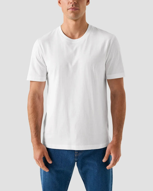 Klassisk vit T-shirt herr med rund hals, kort ärm, och blå jeans mot ljus bakgrund.